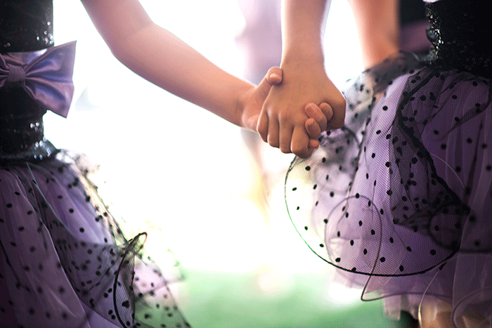 Two young ballerinas in costume holding hands