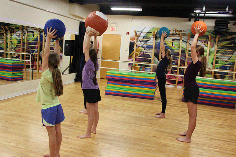 Students in Dance Conditioning class raising practice balls above their heads